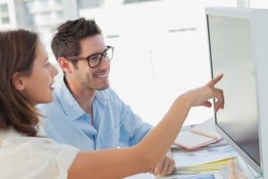 Attractive photo editor pointing at the computer screen while working with a colleague